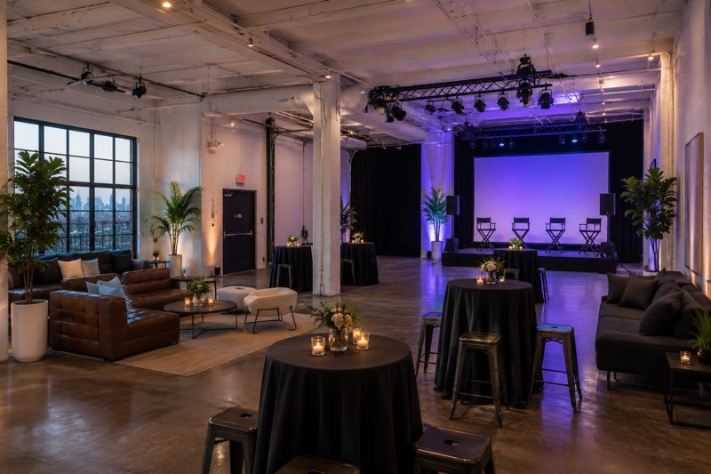 Bright New York loft event venue arranged for private dining with exposed brick, large windows, lounge seating, and reception tables
